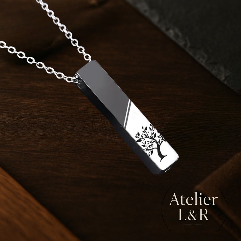 Pendentif en acier inoxydable gravé d’un arbre de vie, photographié en angle sur fond bois, bijou Atelier L&R.